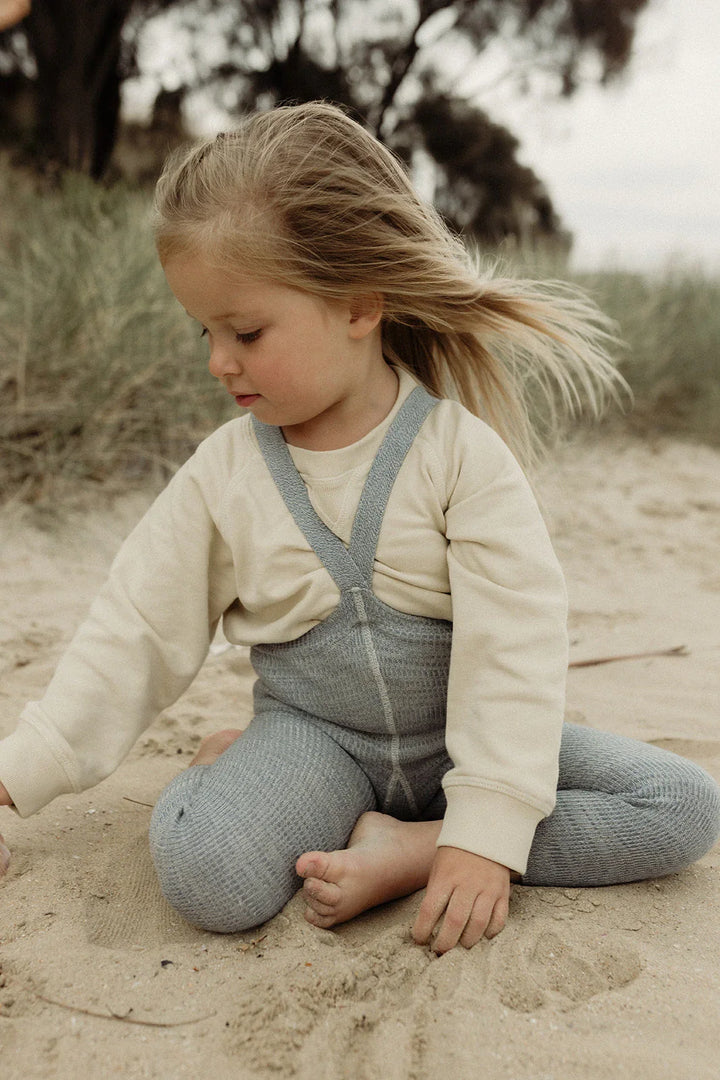 Liten jente i myke barneklær og ullbukser spiller i sanden, bærekraftig babyutstyr for 0-8 år
