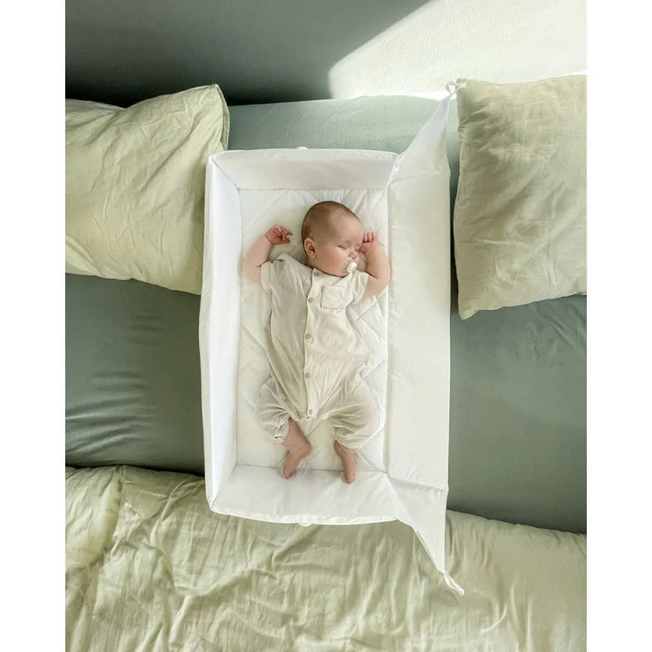 Søvende baby i hvit sengeseng på grønn seng, myk barneklær og babyutstyr