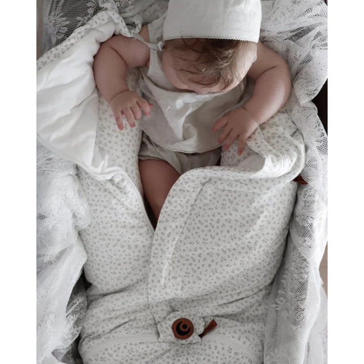 Søvende baby i myk, blomstermønstret sengetøy og hatt, perfekt for nyfødte og små barn