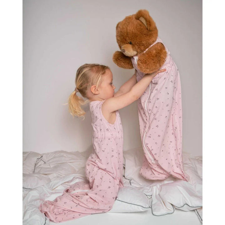 Liten jente i rosa blomsterpyjamas med nattesekk for bjørn, myk barneklær for 0-8 år