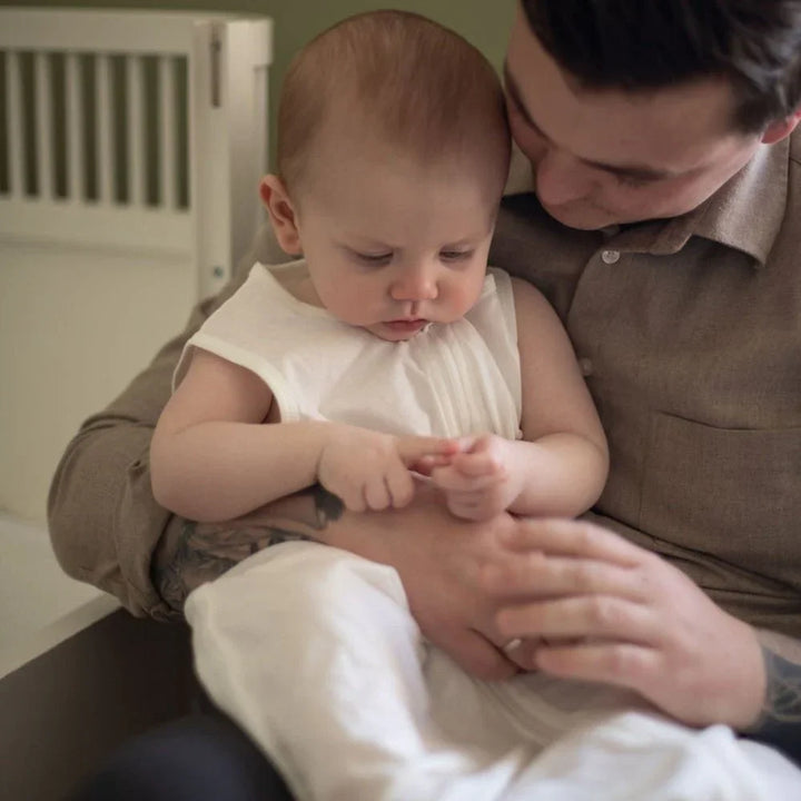 Baby i hvit barneklær holdt av voksen, myk ull og komfortabel babyutstyr for spedbarn