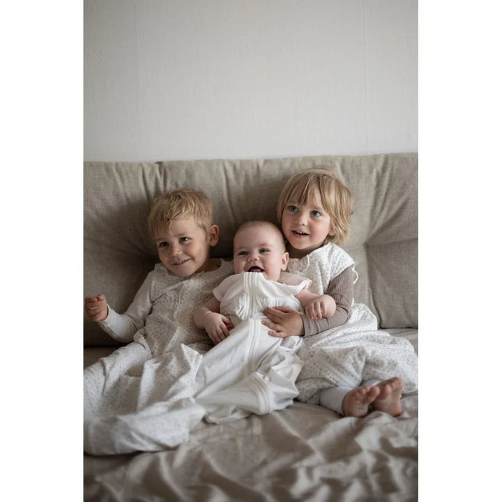 Tre små barn i myke barneklær og babydrakter, kose seg sammen på sofa