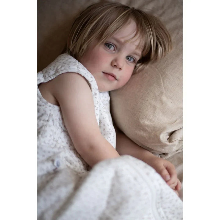 Liten jente i myk barneklær med blomstermønster, hvilende på pute. Bærekraftig babyutstyr for 0-8 år.