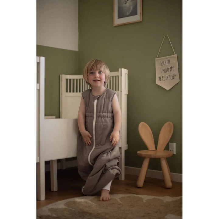 Barn i grå sovepose, myk barneklær for 0-8 år, bærekraftig babyutstyr i hyggelig rom