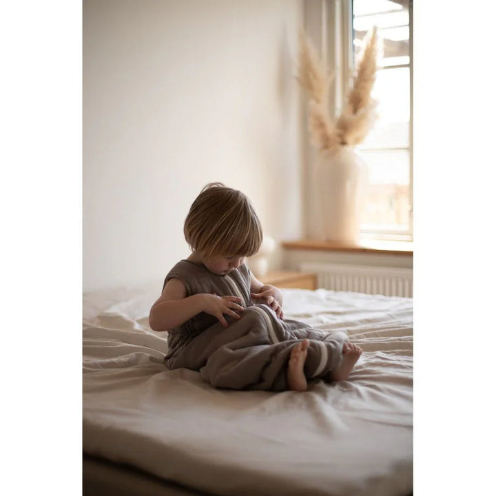 Liten gutt i myk, grå barneklær sitter på seng, perfekt for babyutstyr og ullklær 0-8 år