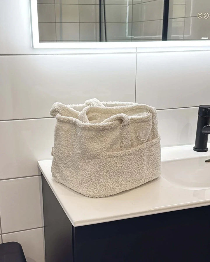 Myk, beige teddybæretaske for babyutstyr på baderomsbord