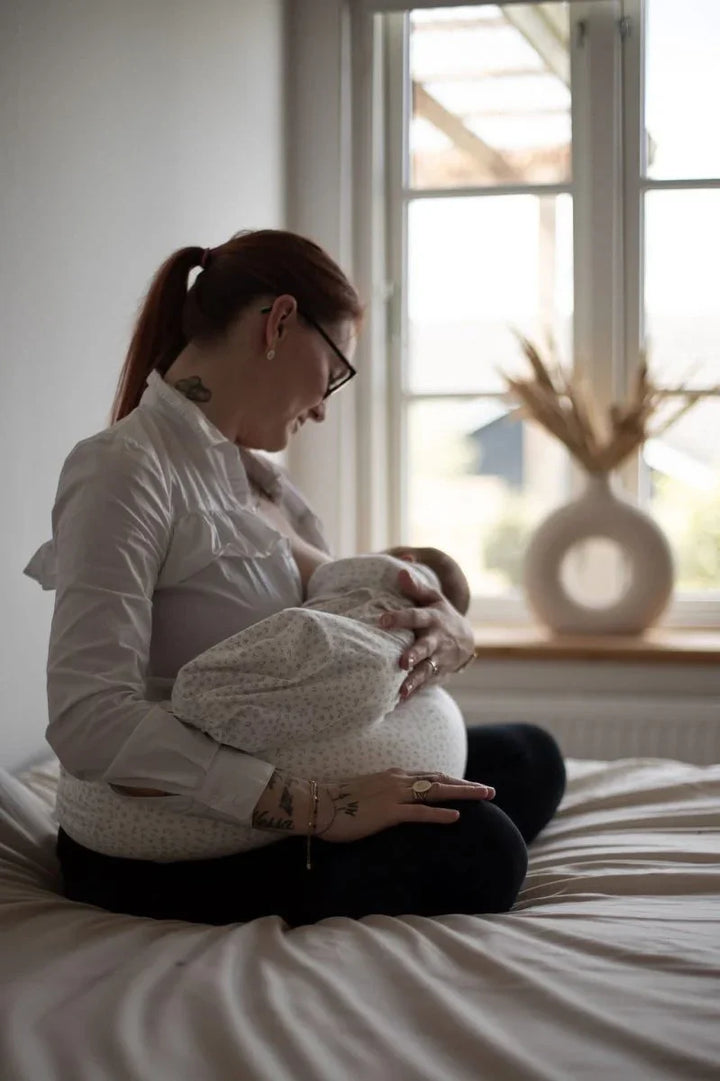 Mor holder nyfødt baby i myk barneklær ved vindu, bærekraftig babyutstyr for 0-8 år