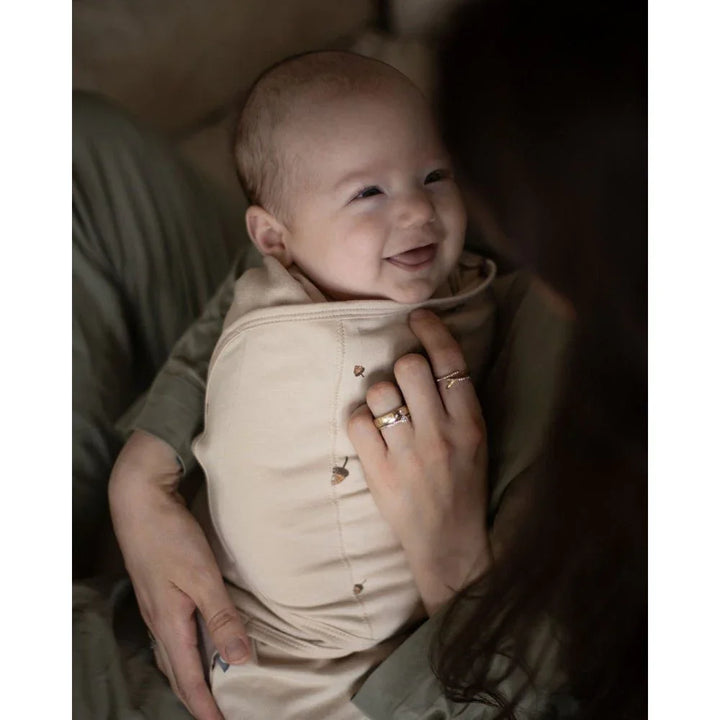 Smilende baby i myk beige barneklær med nøttemotiv, holdt i varm klem
