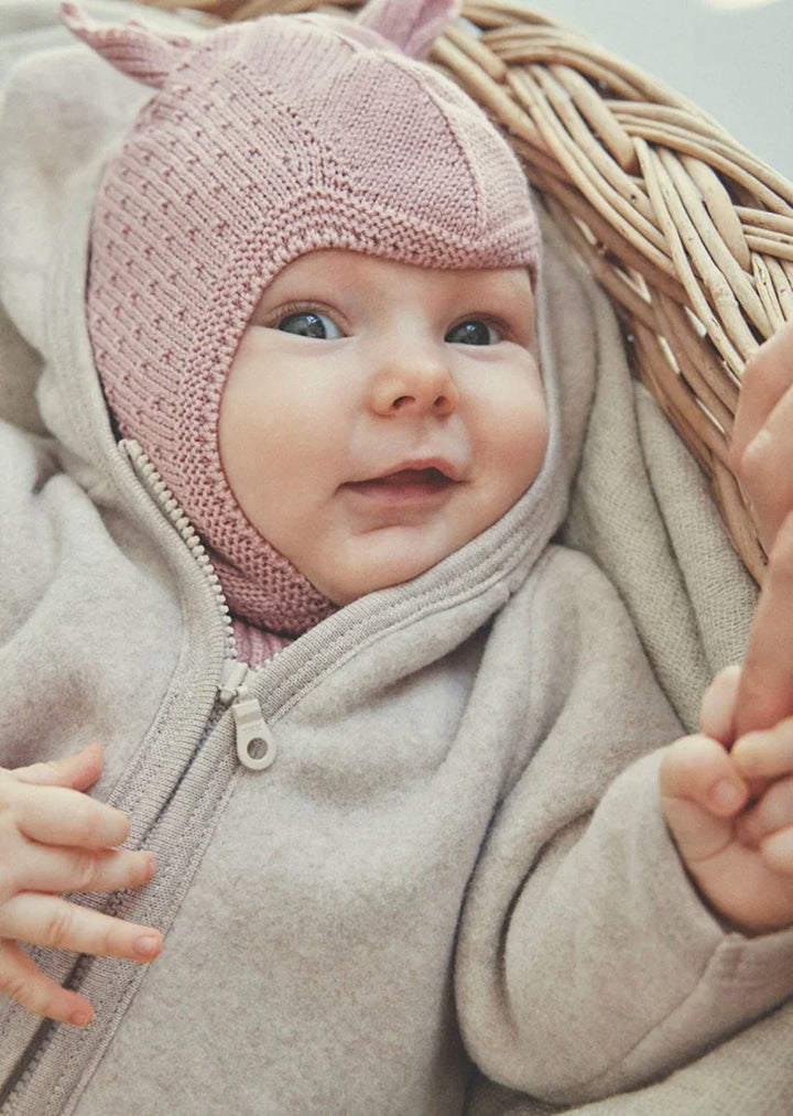 Liten baby i myk ulljakke og rosa strikket lue med ører, perfekt barneklær for små barn.