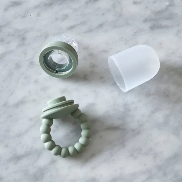 Mintgrønn silikonbabytannring og flaskekomponenter på marmor