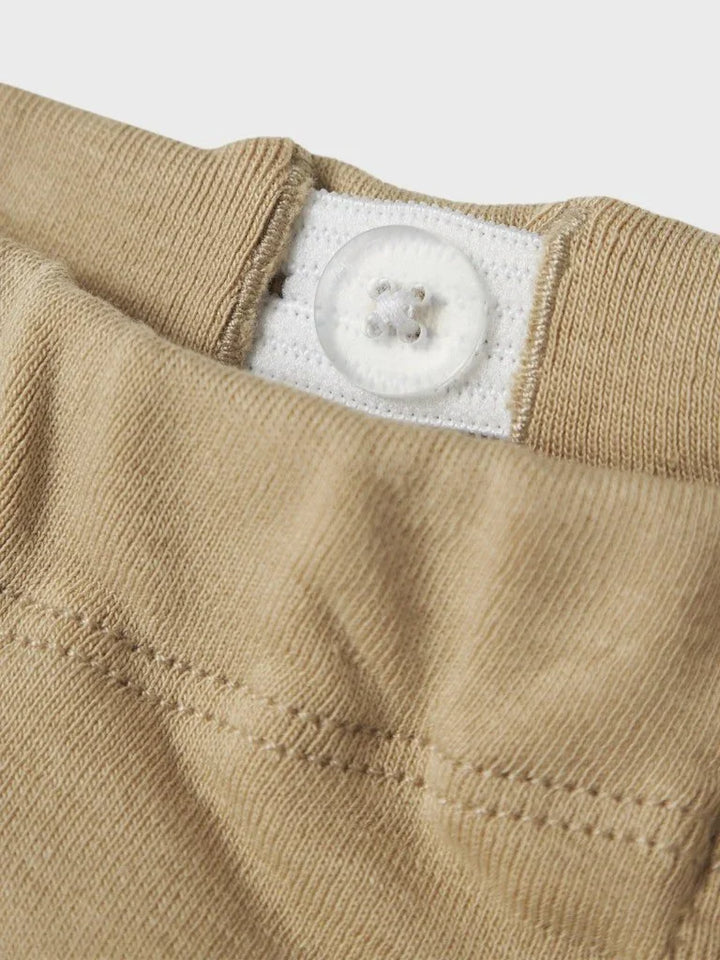 Beige barnetøy med knapp og hvit etikett, myk tekstil for spedbarn og småbarn
