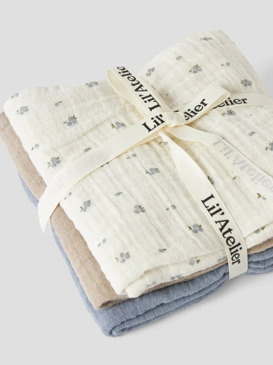 Myke muslin babykluter i blå, beige og hvit med blomstermønster, bundet med Lil’Atelier-ribe