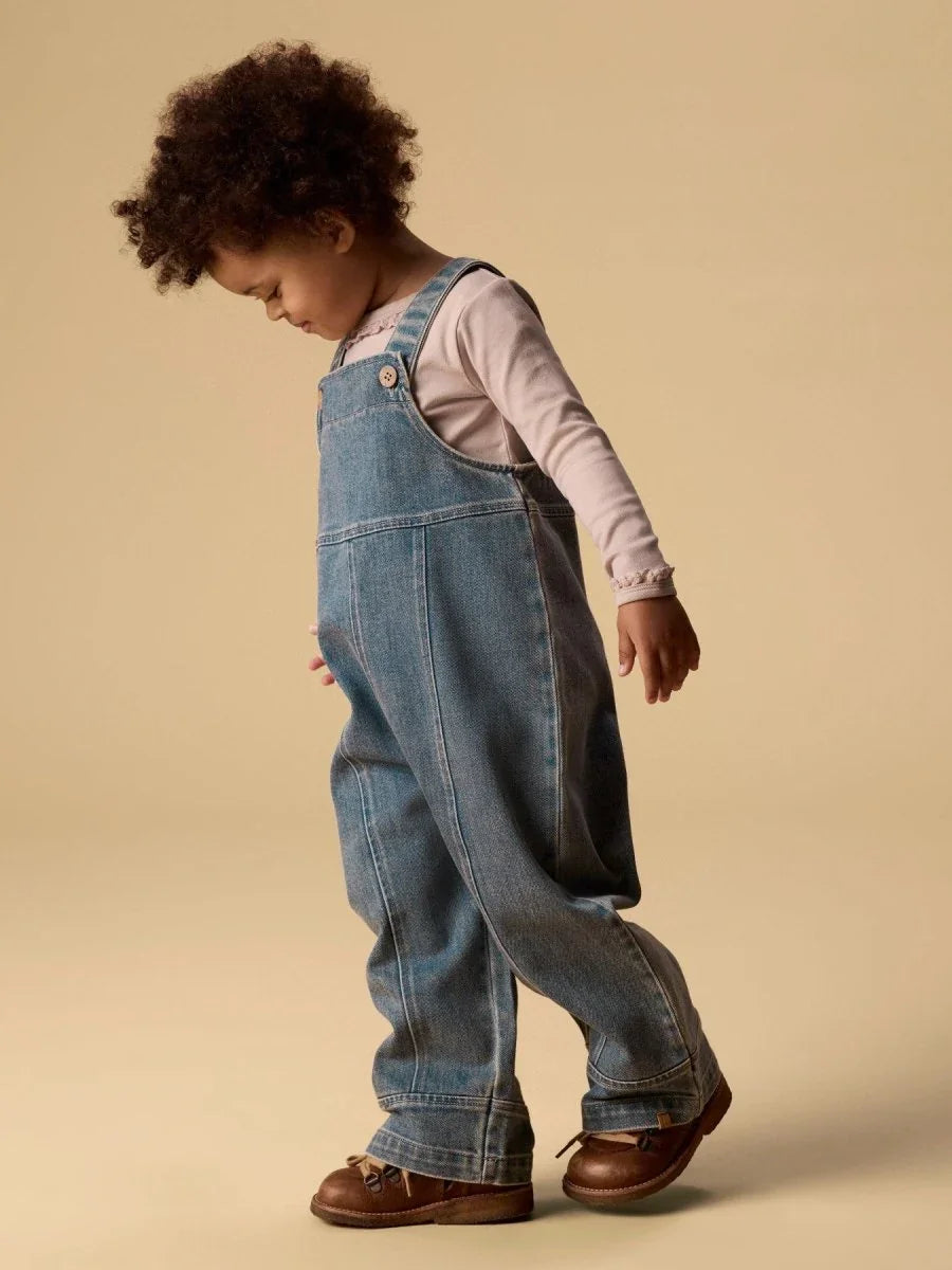 Liten gutt i blå jeansoveralls og brun sko, myk barneklær for 0-8 år