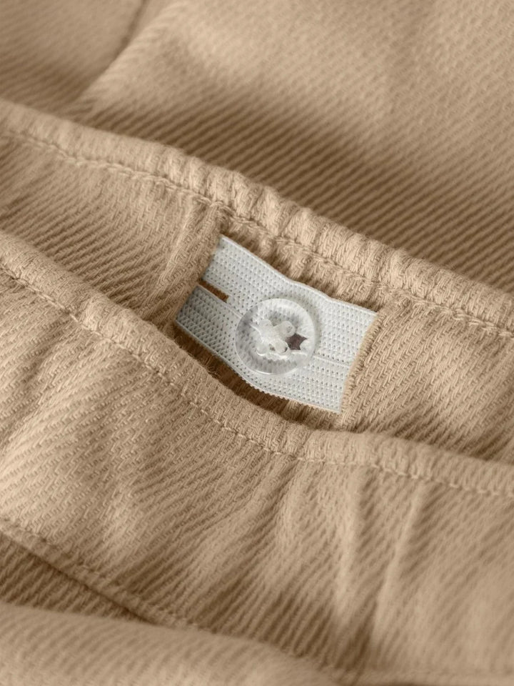 Beige barneklær i myk ull med hvit knapp og elastisk liv