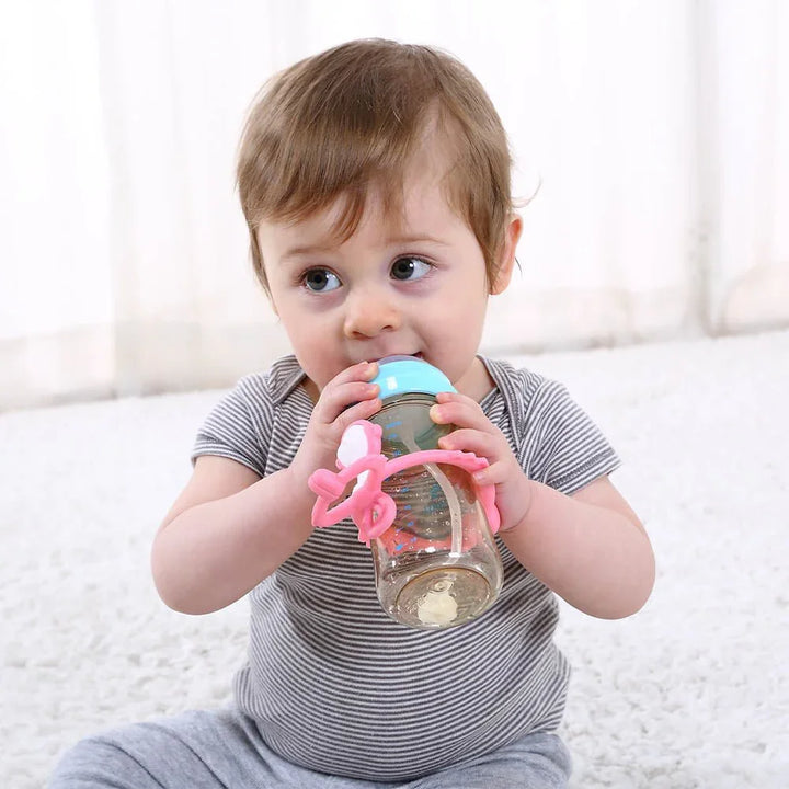 Liten baby drikker fra flaske med rosa grep, myk barneklær og babyutstyr for 0-8 år