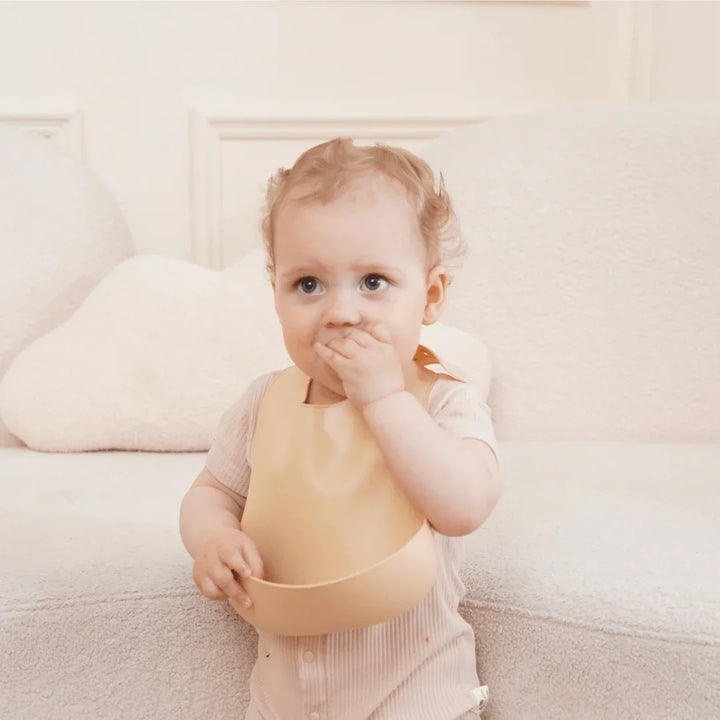 Baby i myk, beige spisekåpe på sofa, barneklær 0-8 år