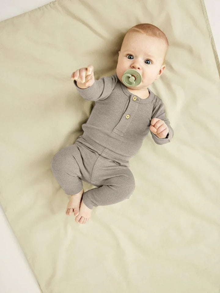 Baby i myk, grå ullpyjamas med knapper, liggende på sengetøy. Perfekt barneklær for spedbarn.