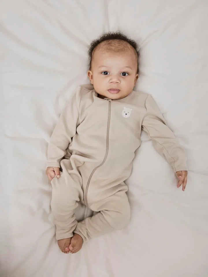 Baby i myk beige onesie med bjørnemotiv, perfekt for nyfødte og små barn