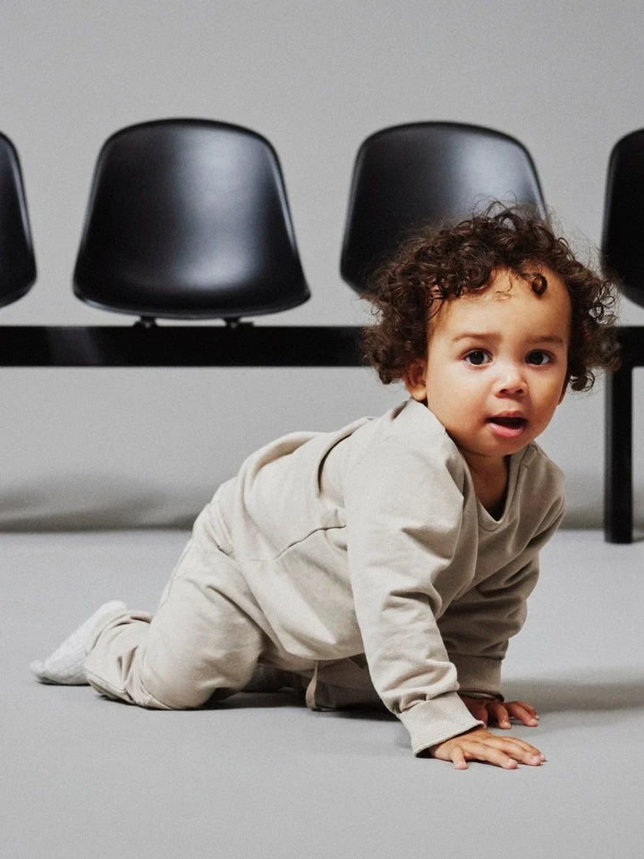 Baby i myk beige treningssuit kryper på gulv, perfekt barneklær for små barn