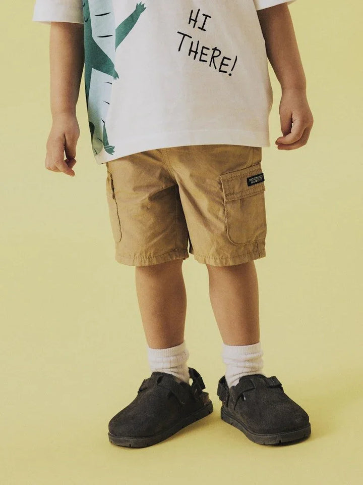 Barn i beige cargo shorts, hvit T-skjorte med &