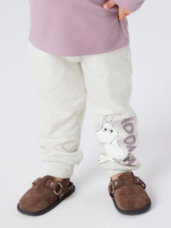 Barn i lysgrå bukser med Moomin-trykk, lilla langærmet topp og brune sko