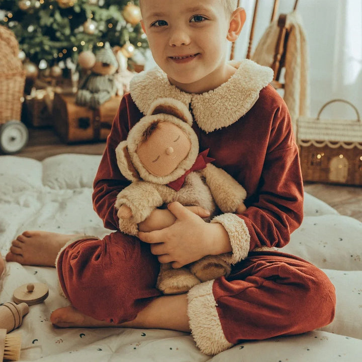 Barn i myke, røde pyjamas med plysjkant, holder plysjdyr foran juletre. Perfekt barneklær for jul.