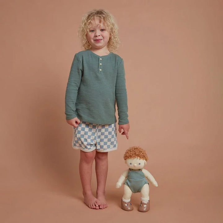 Liten gutt i grønn langærmet topp og sjakkmønstret shorts med dukke, barneklær 0-8 år