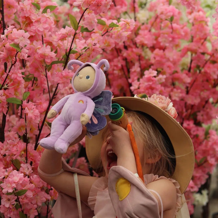 Liten jente med lilla myk plysfigur og teleskop foran rosa blomster, barneklær 0-8 år