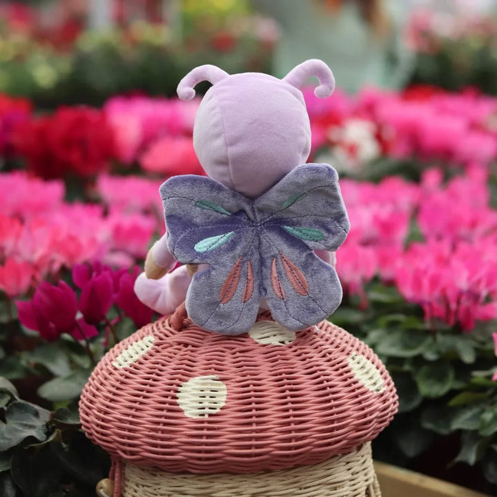 Lilla plysfigur med sommerfuglvinger på rødmuslingkorg, blomsterbakgrunn