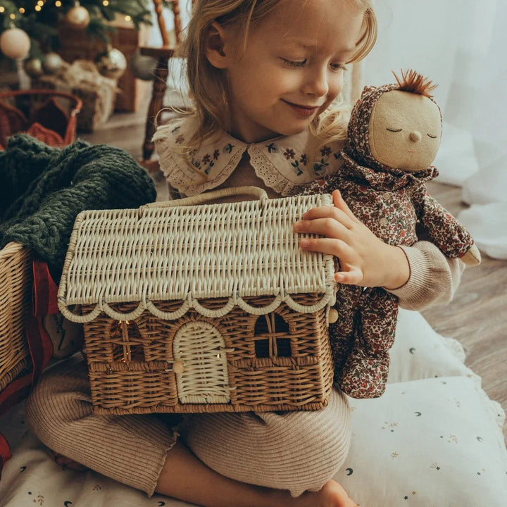 Liten jente med dukke og vevd husleke, myke barneklær og julestemning