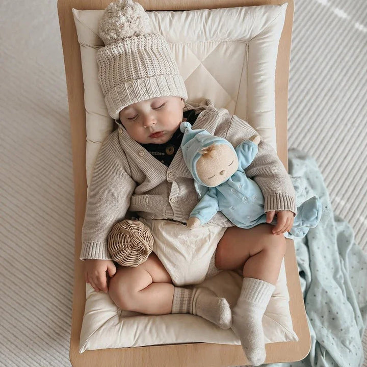 Søvende baby i myk ullgenser og lue, med blå dukke – perfekt barneklær for små barn