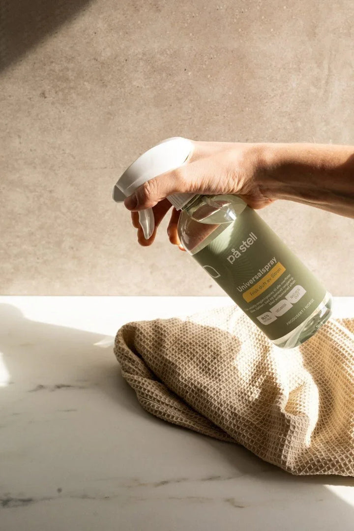 Hånd som sprayer på stell universalspray med sitronduft på tekstil, miljøvennlig rengjøring