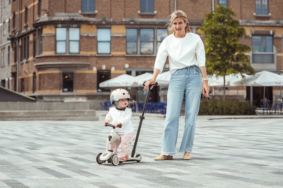 Mor og baby på sparkesykkel i byen, myke barneklær og sikkerhetsutstyr for små barn