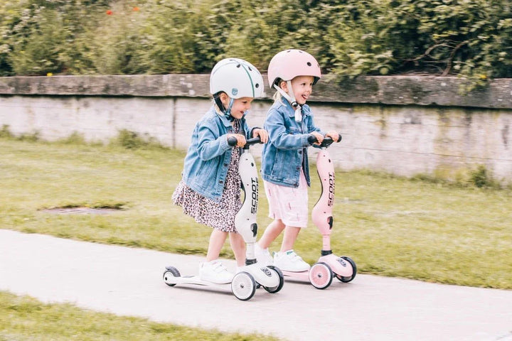 To små barn på sparkesykler med hjelmer, utendørs på sti. Barneklær, trygg lek for 0-8 år.