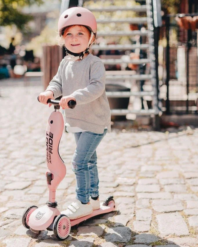 Liten jente på rosa sparkesykkel med hjelm, barneklær og lekeutstyr for små barn