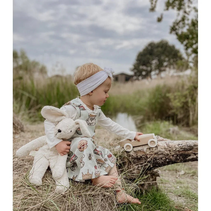 Liten jente i myk barneklær med kanin og trebil ute i naturen