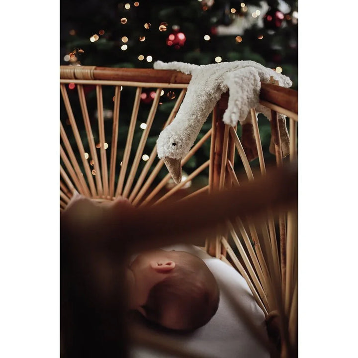 Søvende baby i råttestol med myk svaneknuffe, juletre i bakgrunn – barneklær og babyutstyr