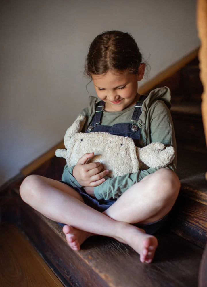 Liten jente i overalls og grønn genser sitter på trapp med plysdyr, myke barneklær for 0-8 år
