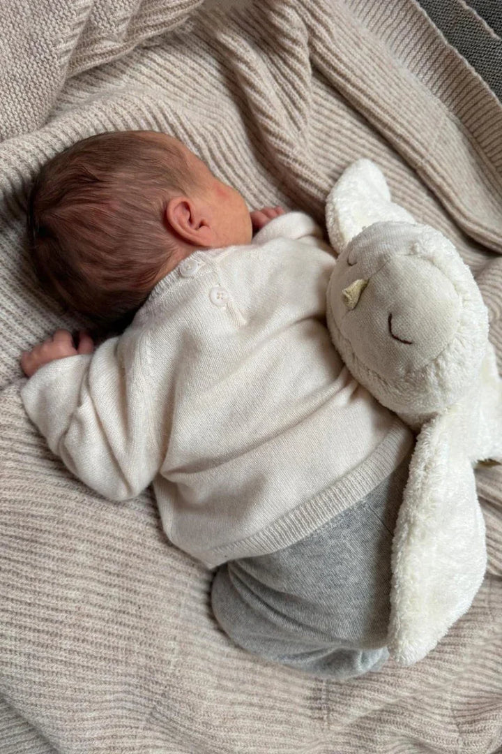 Nyfødt i myk ullgenser med kaninpynt, hvit babyklær og grå bukser på strikket dekken