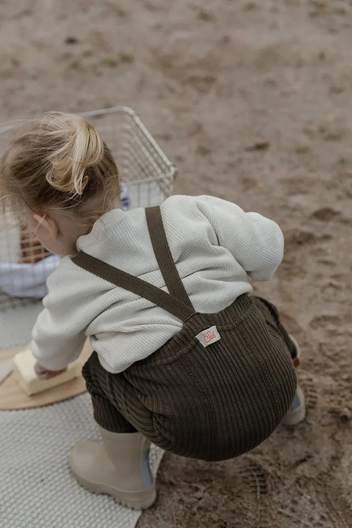 Liten gutt i myke barneklær og corduroy bukser, leker på sand med korg