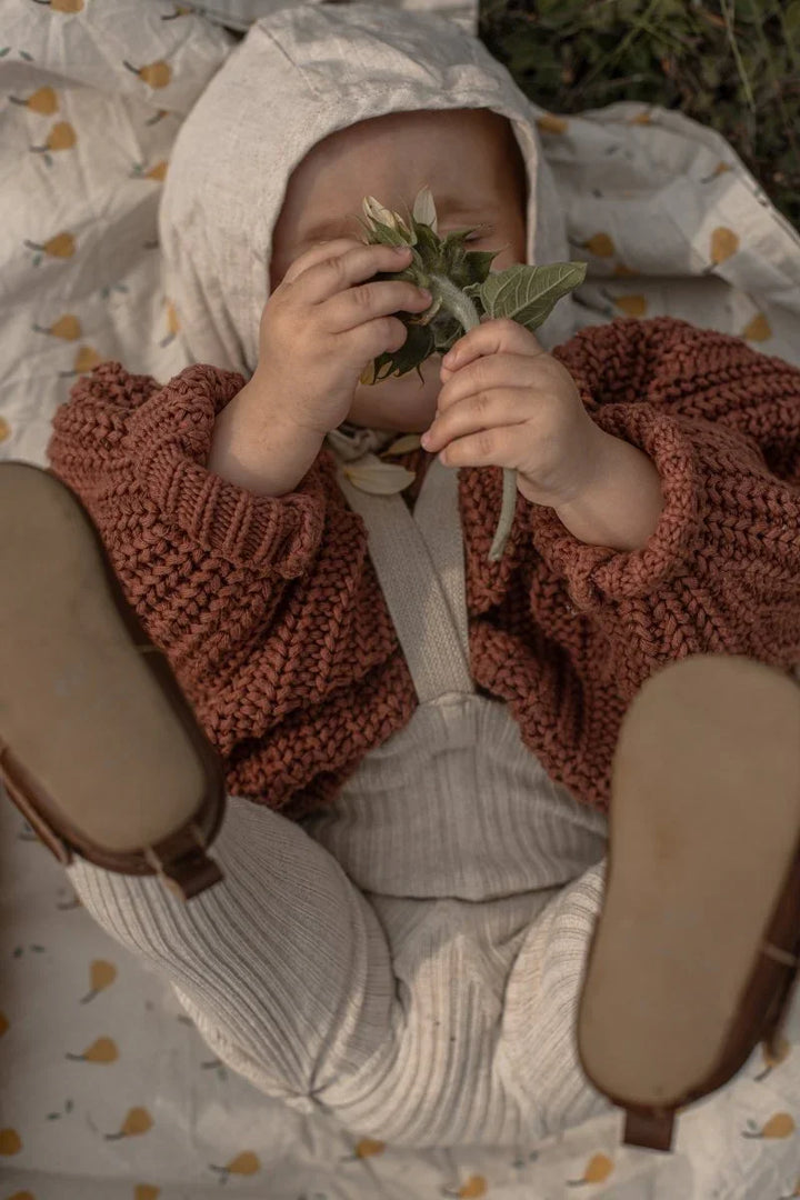 Baby i myk ulltrøye og bukse, leker med blomst ute. Bærekraftig barneklær for 0-8 år.