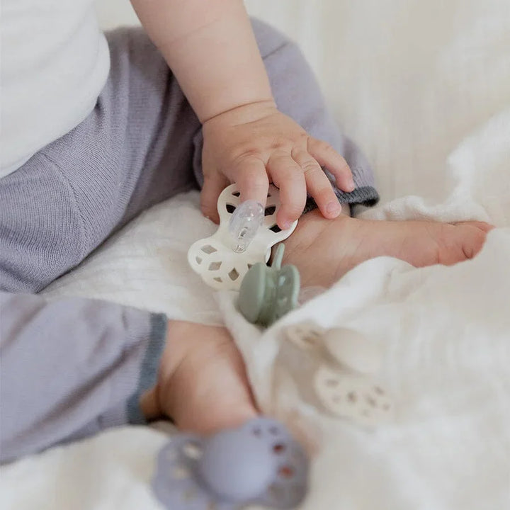 Baby i myke ullbukser holder på en silikonepatt, med flere pattar på hvit pute