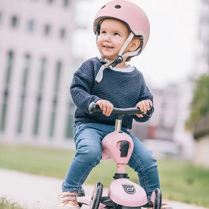 Liten gutt på rosa barnebil med hjelm, barneklær og jeans, utendørs lek