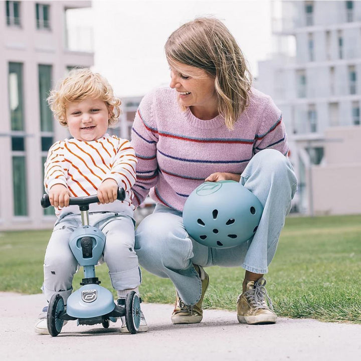 Liten gutt på blå trille sykkel med mor som holder hjelm, utendørs lek for spedbarn og småbarn